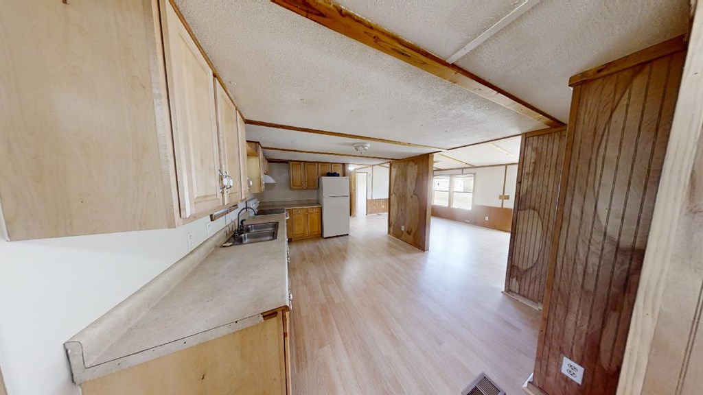 Open kitchen and living area with wood cabinets, paneled walls, and light flooring.