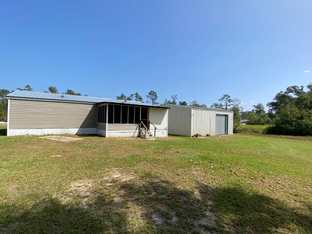 Single-story home with a screened porch and adjoining metal garage on a grassy lot.