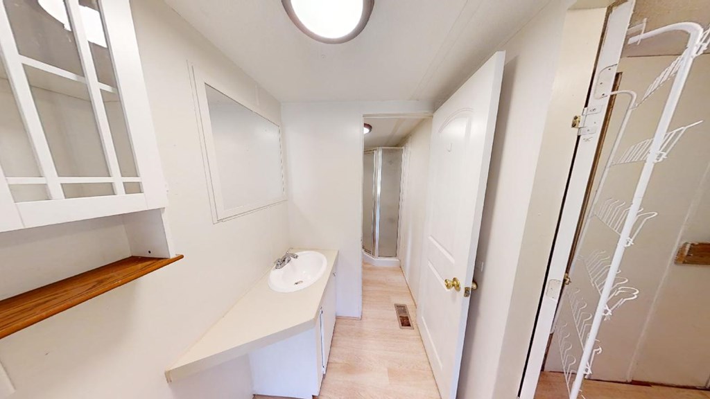 Narrow bathroom with a long vanity, wall cabinets, and a shower at the far end.
