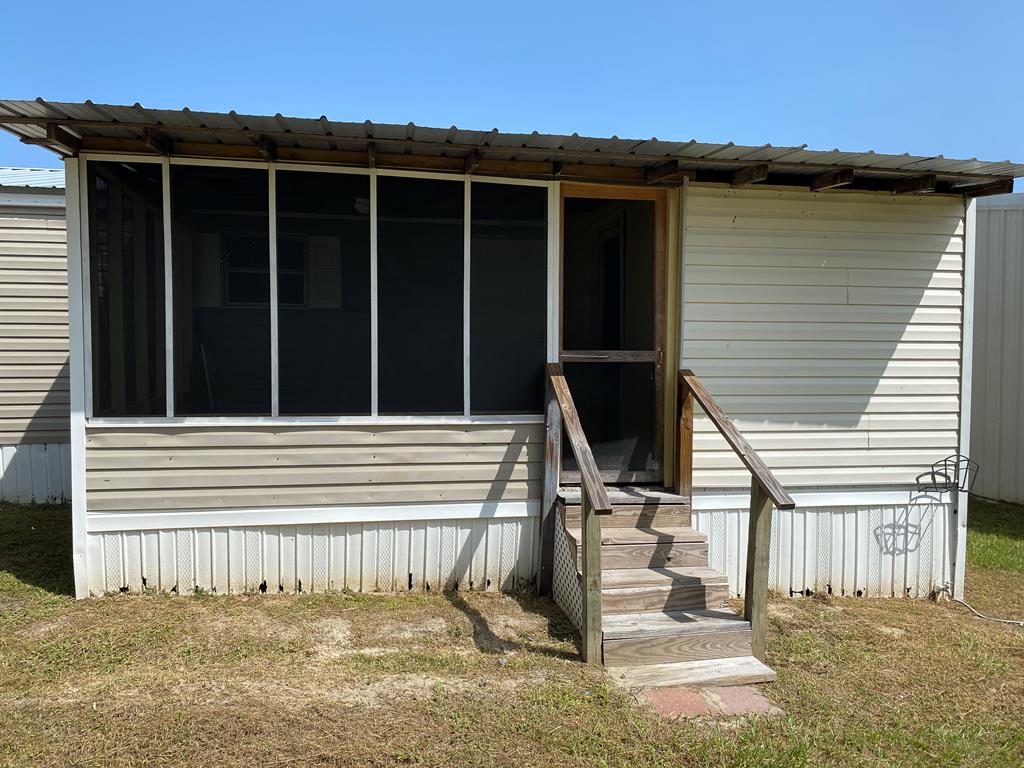 Manufactured home exterior with screened porch, metal awning, and wooden entry steps.