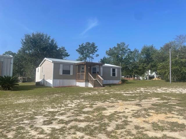 Manufactured home with gray siding and a small covered porch on a sandy, sparsely grassed lot.