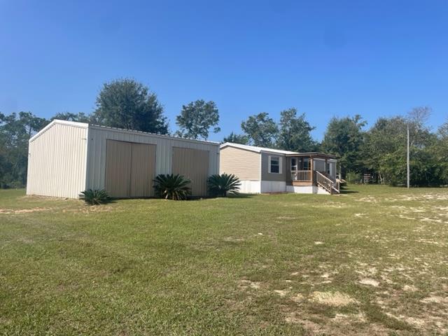 Light-colored manufactured home with a metal-sided garage, raised porch, and broad grassy yard.