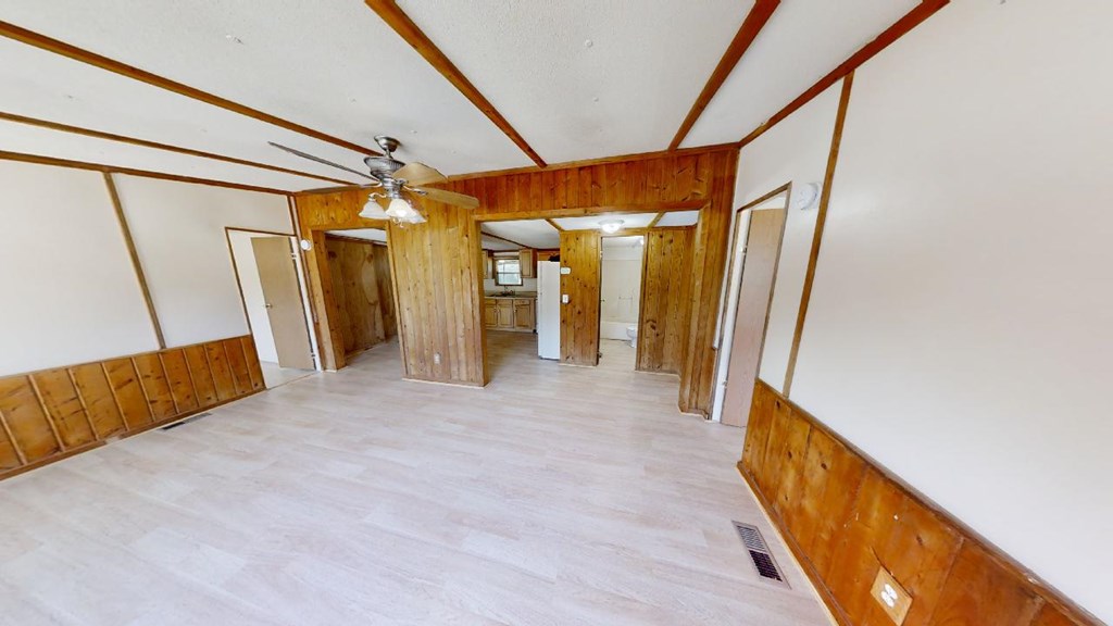 Empty living room with wood-paneled walls, exposed ceiling beams, and a ceiling fan.