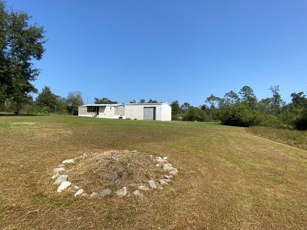 White metal outbuildings sit across a broad grassy lot, with a ring of stones in the foreground.