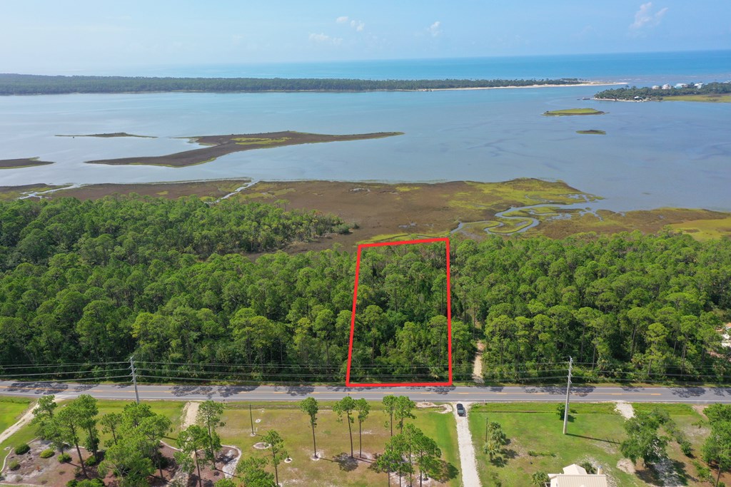Aerial view of wooded lot outlined in red, with road frontage and coastal bay beyond.