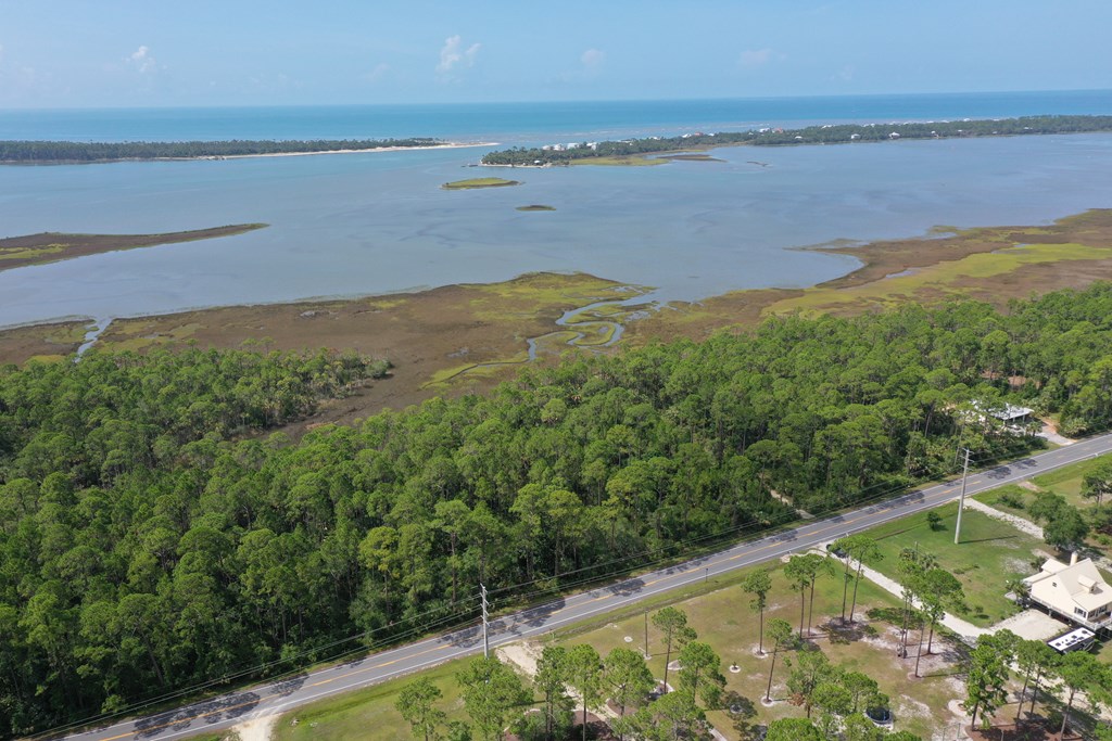 Aerial view of wooded property beside a road, coastal marshes, and a broad bay.