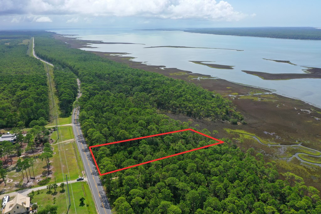Wooded lot outlined in red beside a road, with coastal marsh and water beyond.