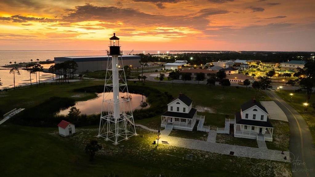 Waterfront property with a tall lighthouse tower and two white cottages at sunset.