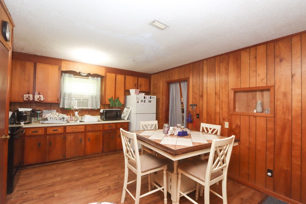 Wood-paneled kitchen and dining area with white table and chairs, wood cabinetry, and a window air conditioner.