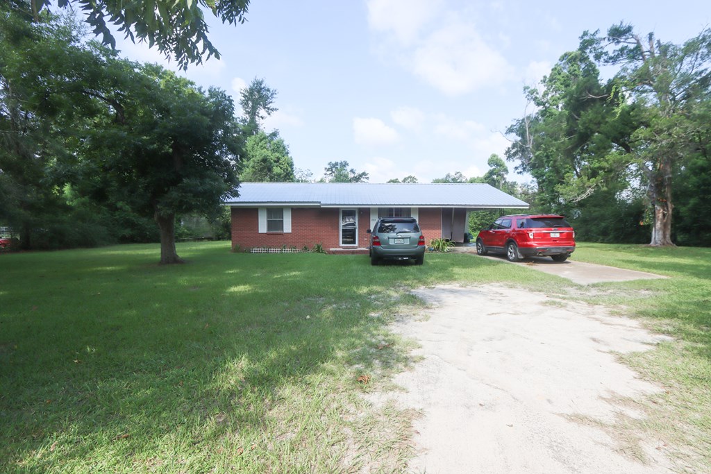 Single-story brick house with a metal roof, broad lawn, driveway, and two parked vehicles.