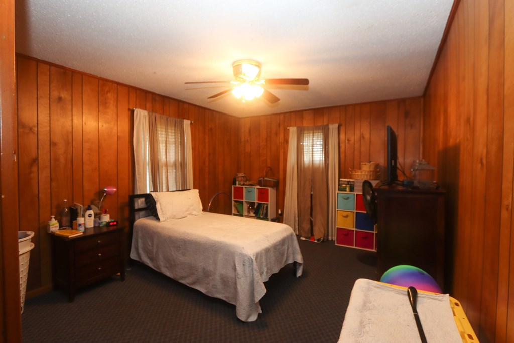 Wood-paneled bedroom with a bed, ceiling fan, curtained windows, and colorful storage cubbies.