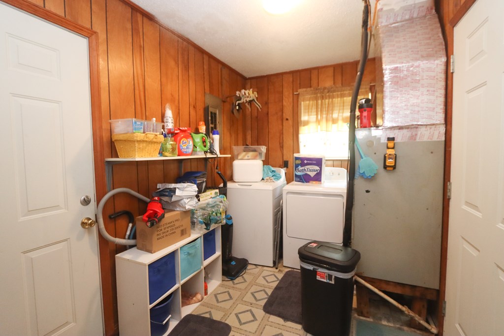 Laundry room with a washer and dryer, wood-paneled walls, and crowded utility shelving.