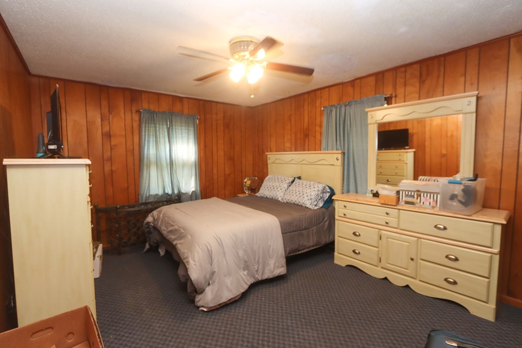 Bedroom with a made bed, cream dresser and mirror, wood-paneled walls, and ceiling fan.