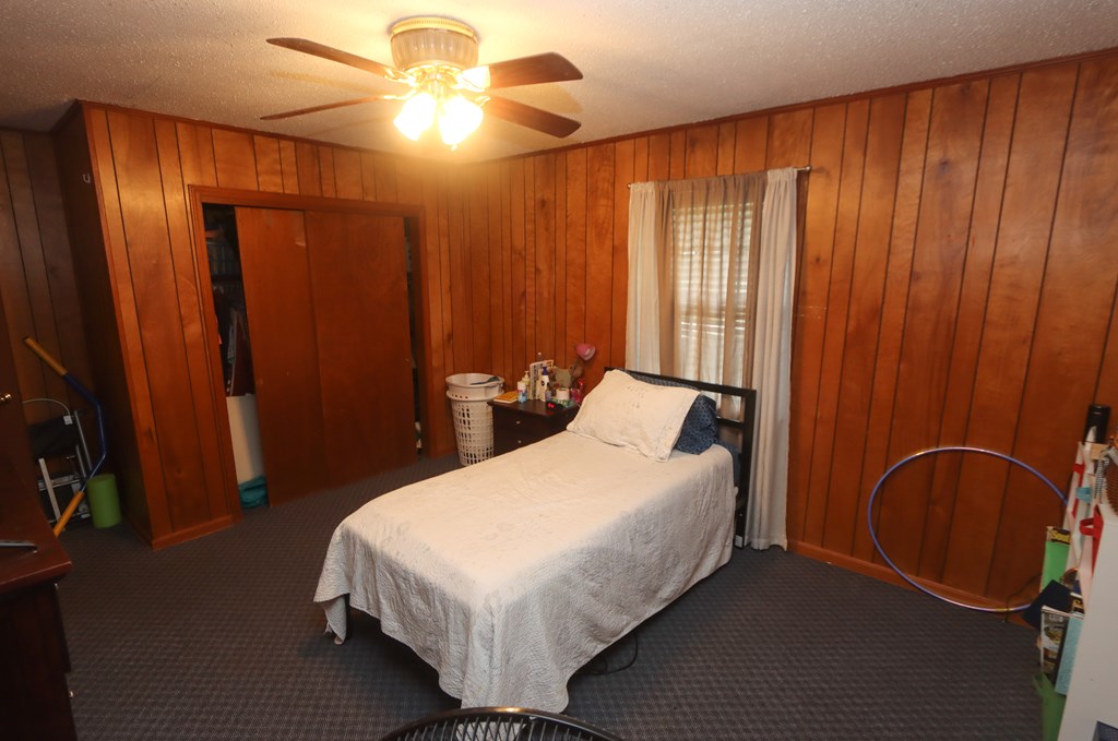 Bedroom with wood-paneled walls, a single bed, and a ceiling fan with light.