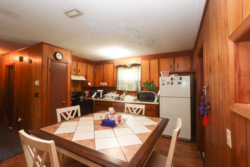 Wood-paneled kitchen with a tiled dining table, white refrigerator, and window air conditioner.