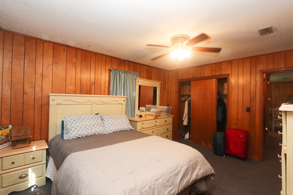 Bedroom with a large bed, wood-paneled walls, dresser, and open closet with luggage.
