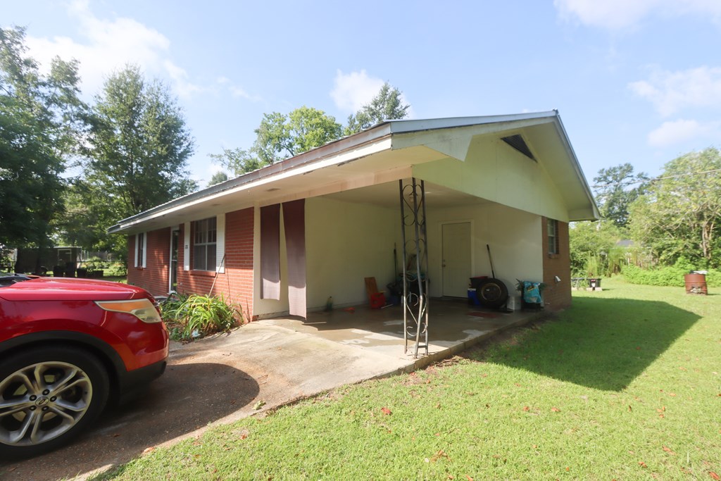 Single-story brick house with a wide covered carport, driveway, and grassy lawn.