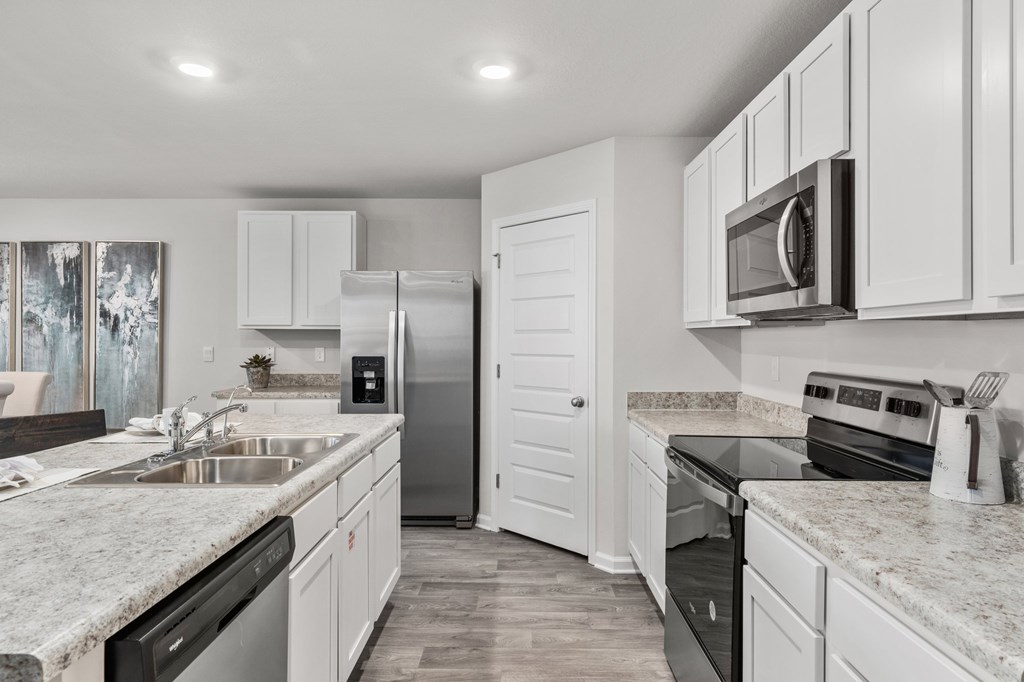 Modern kitchen with white cabinets, gray stone counters, and stainless steel appliances.