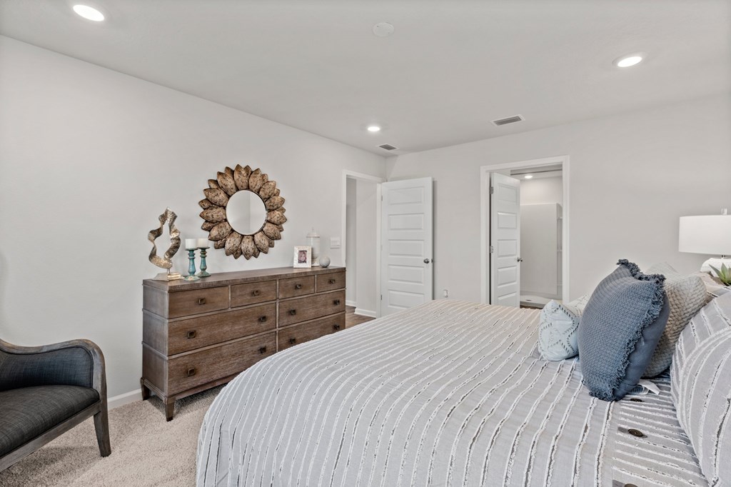 Bedroom with a striped bedspread, blue pillows, and a wooden dresser beneath a sunburst mirror.