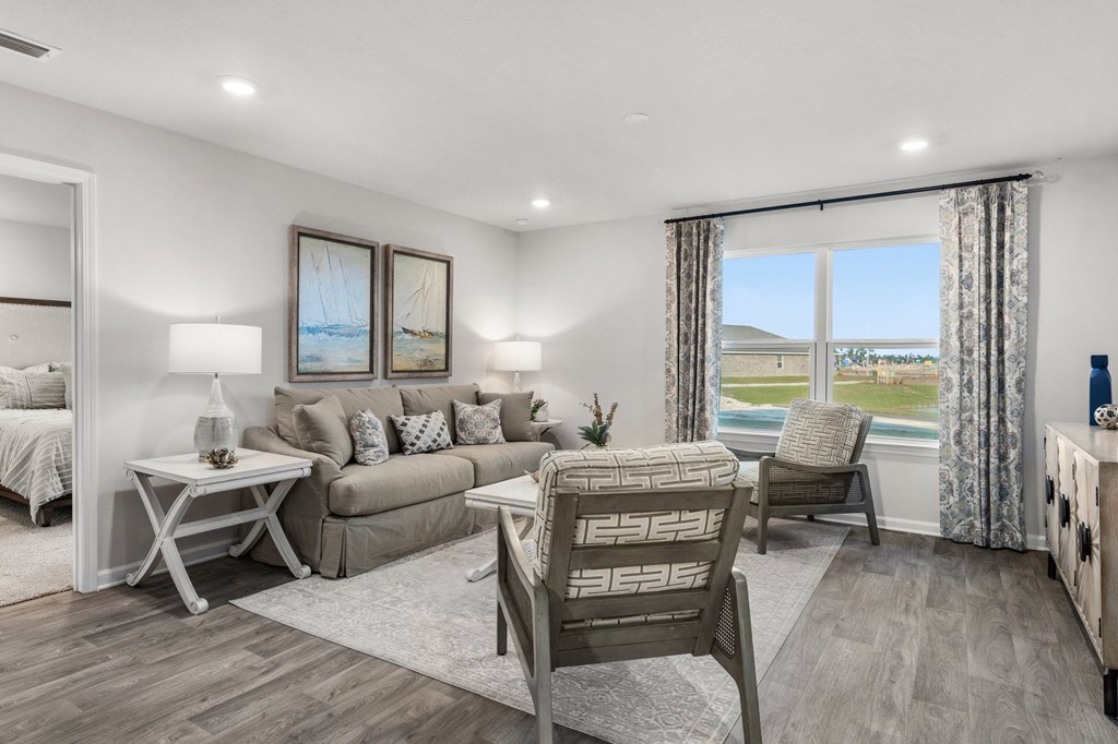 Furnished living room with a neutral sofa and patterned armchairs facing a large window overlooking water.