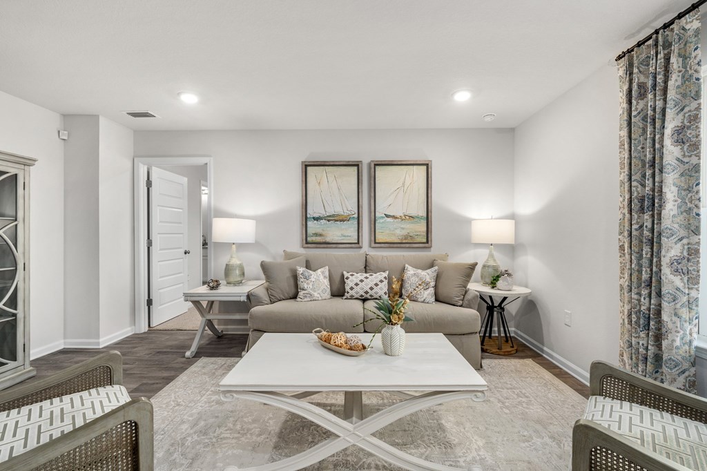 Staged living room with a gray sofa, sailboat artwork, and white coffee table.