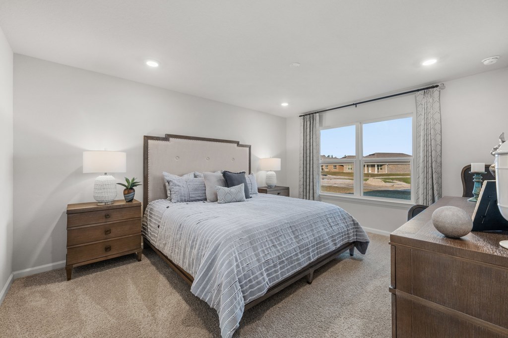 Staged bedroom with a large gray-bedded bed and a window overlooking neighboring homes.