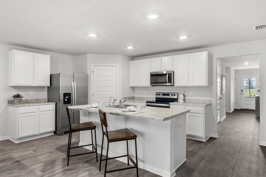 White kitchen with stainless steel appliances and a large stone island with two stools.