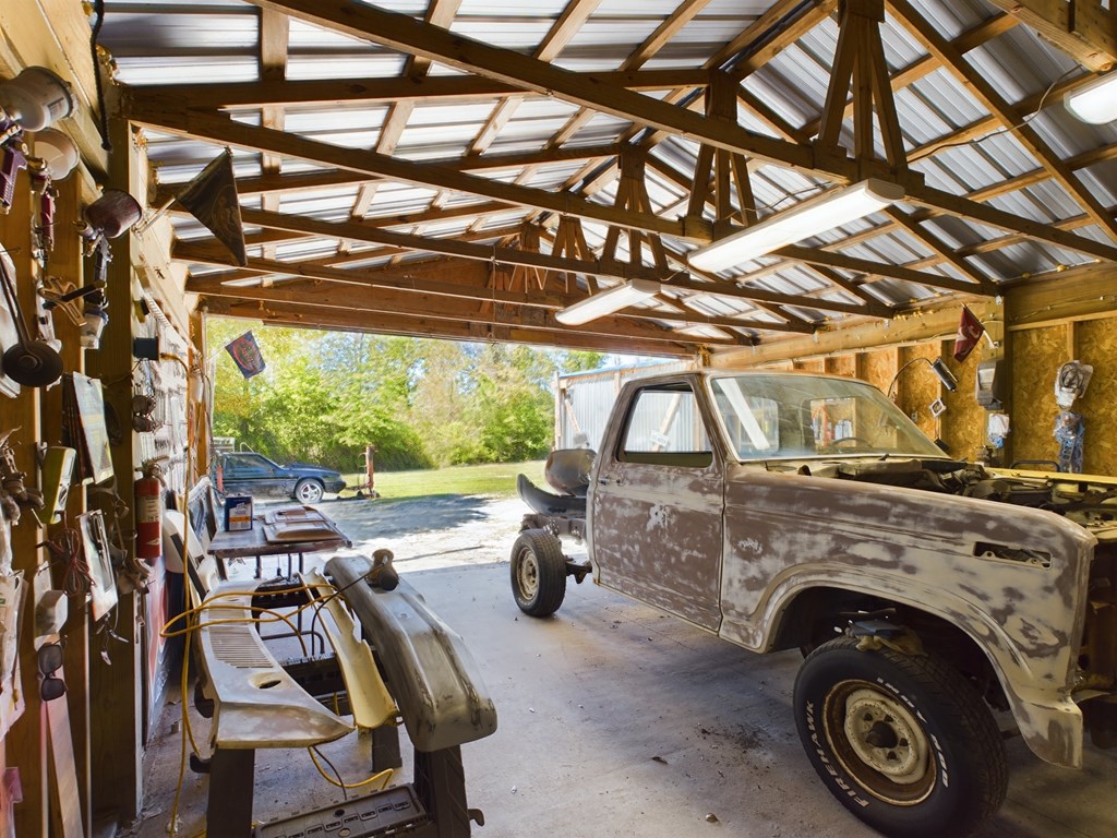 Workshop garage with exposed timber trusses, translucent roof panels, and a weathered vintage pickup.