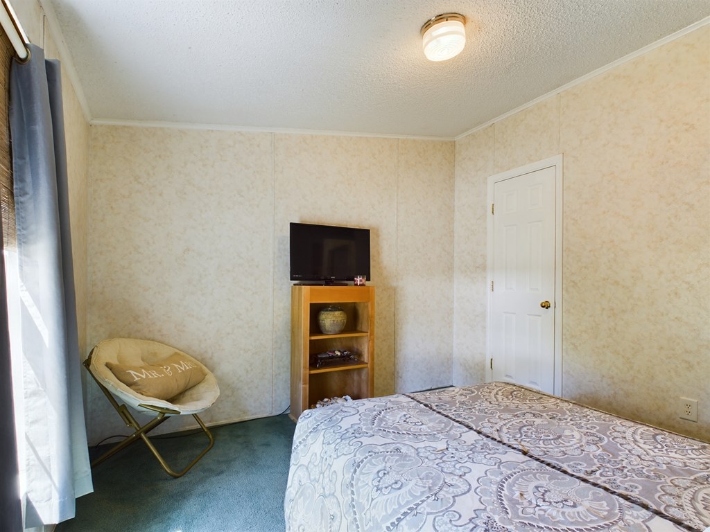 Bedroom with a patterned bedspread, blue carpet, and a television on a wooden shelf.