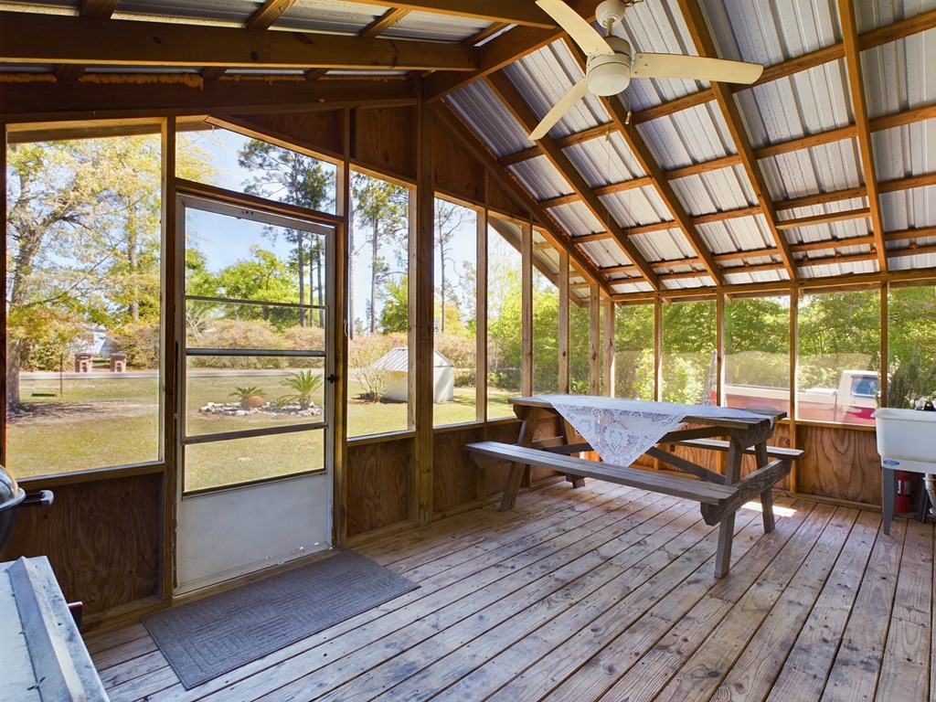 Screened porch with a wooden picnic table, exposed beams, and views of a leafy yard.