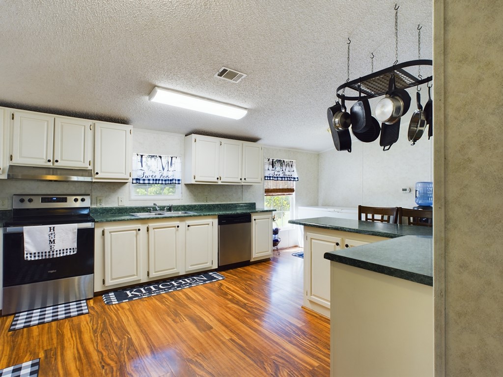 Kitchen with white cabinets, green countertops, stainless steel appliances, and glossy wood-look flooring.