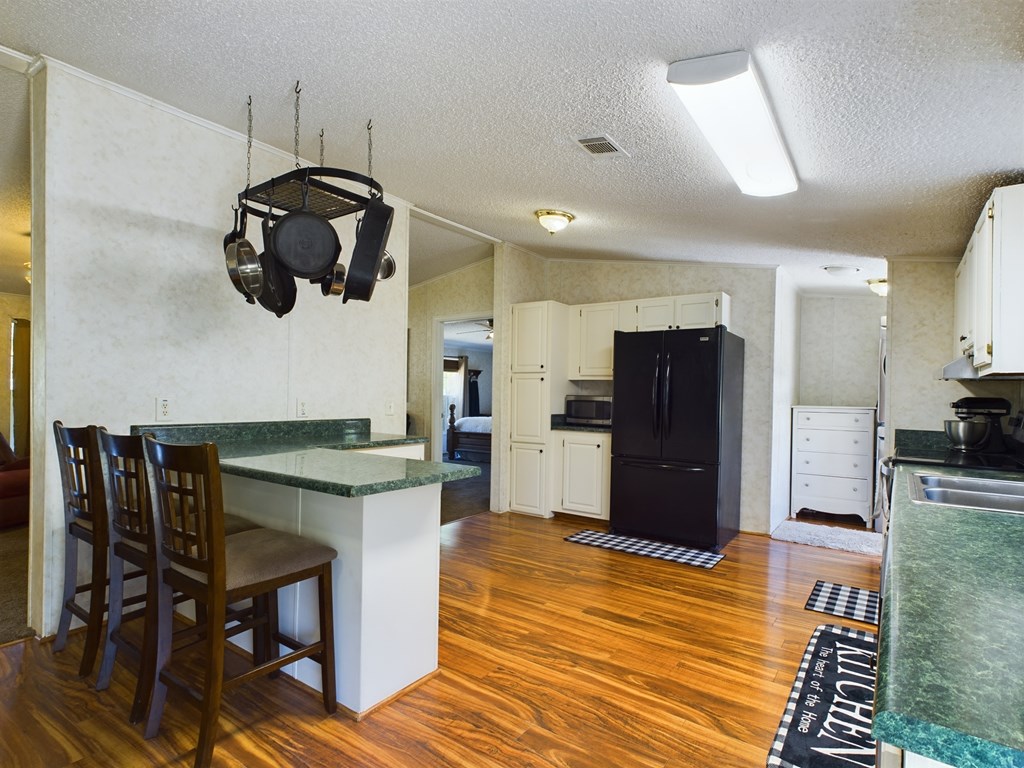 Kitchen with white cabinets, black refrigerator, green countertops, and a breakfast bar with wooden stools.
