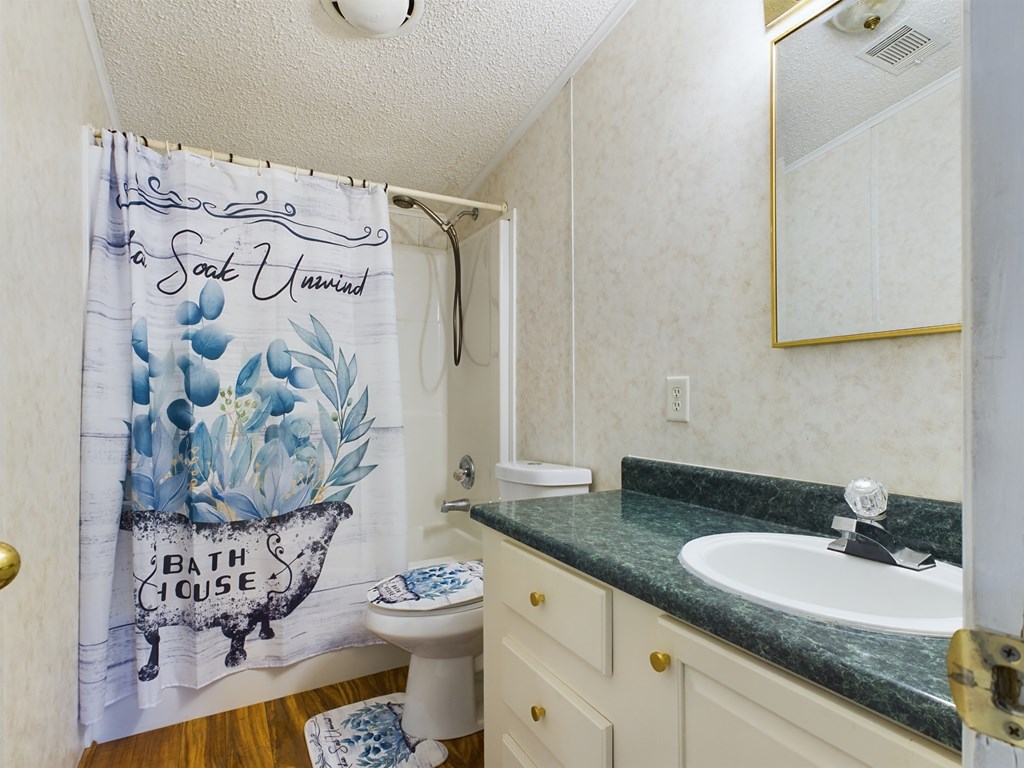 Bathroom with a floral bathtub shower curtain, white toilet, and cream vanity with a dark green countertop.