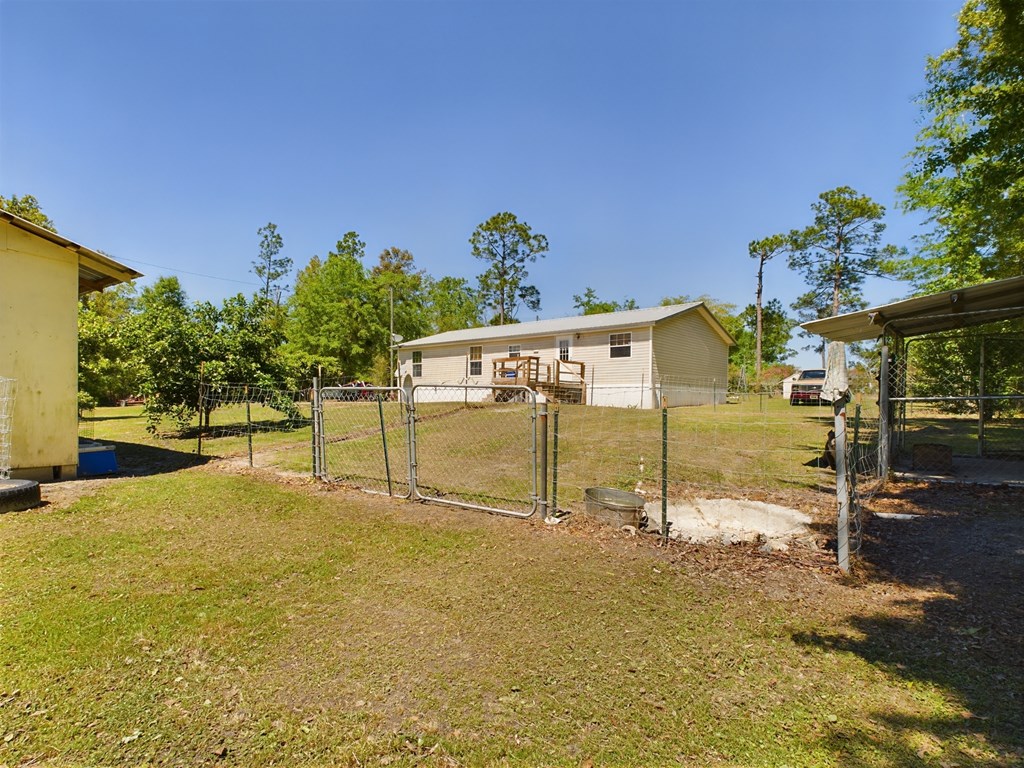 Single-story home behind a chain-link fence, with a small deck and outbuildings.