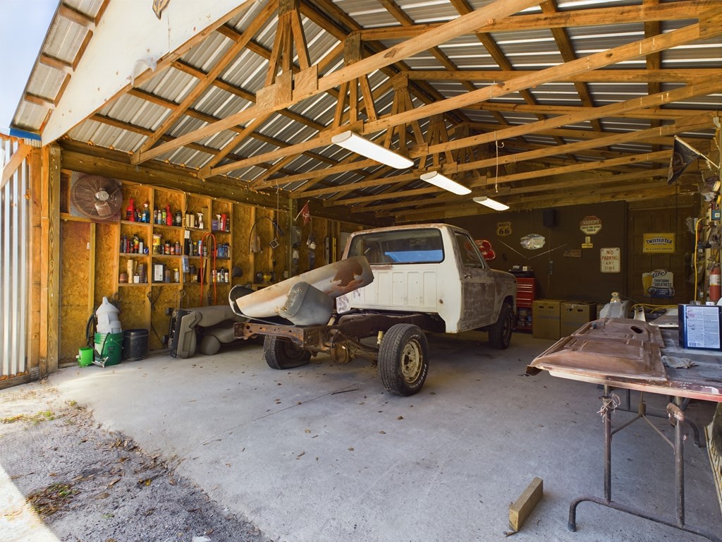 Garage workshop with exposed timber trusses, a vintage pickup truck, tools, and a vehicle body on a stand.