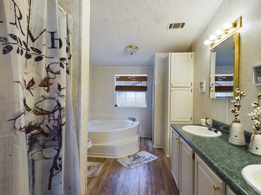 Bathroom with a corner soaking tub, double-sink vanity, gold-framed mirror, and patterned shower curtain.