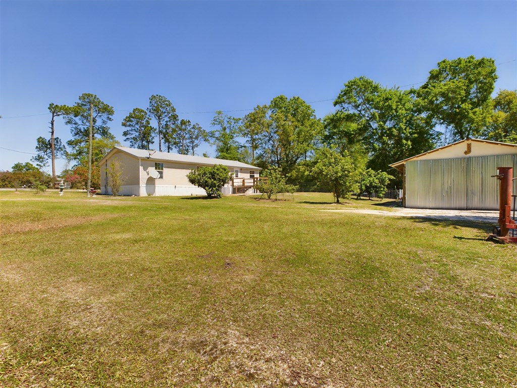 Single-story house and metal outbuilding across a broad grassy yard with mature trees.