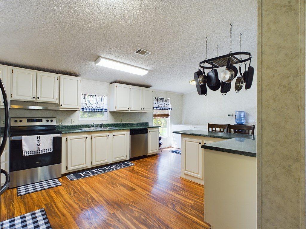 Kitchen with white cabinets, green countertops, stainless steel appliances, and a hanging pot rack.