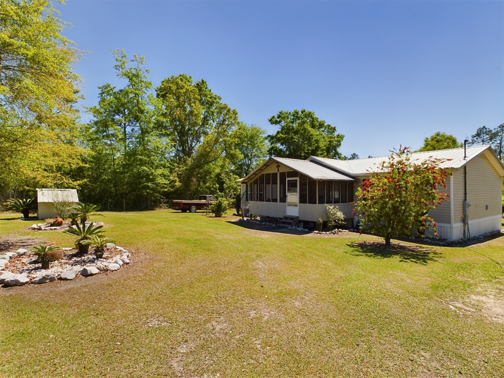 Single-story home with a screened porch, broad grassy yard, and mature trees.