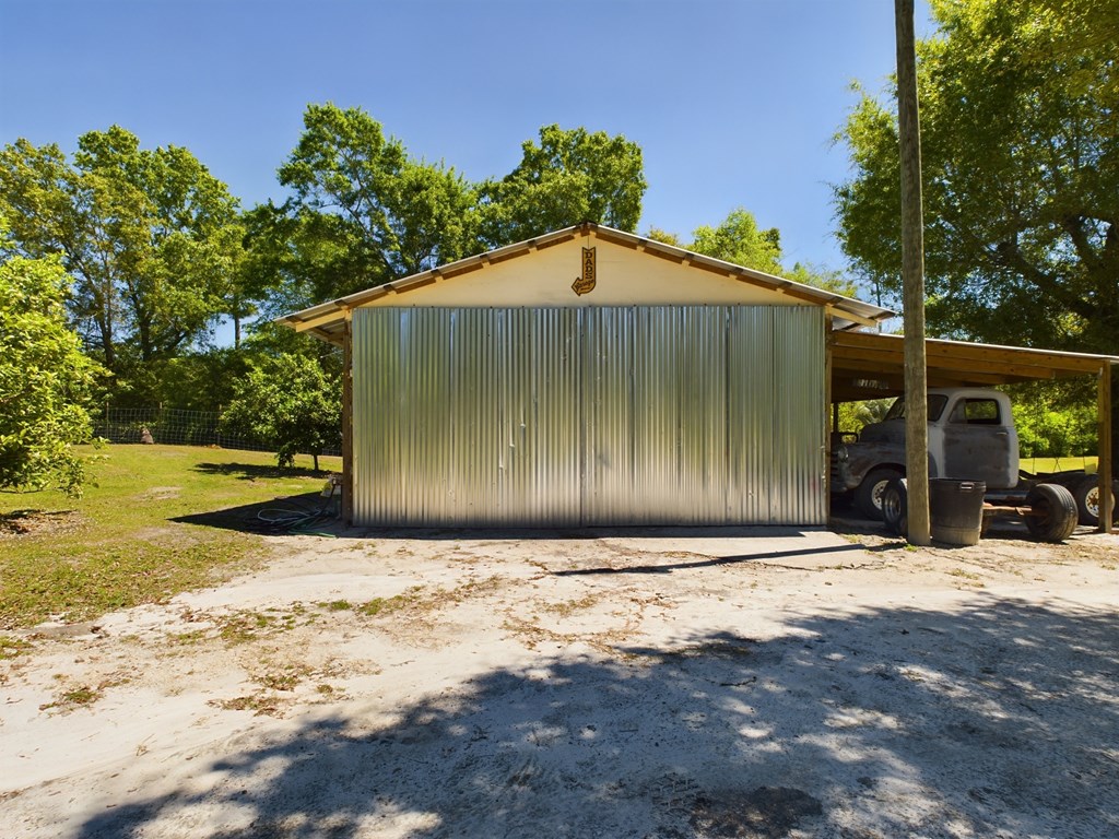 Metal-sided garage with wide sliding doors and an attached carport sheltering a pickup truck.
