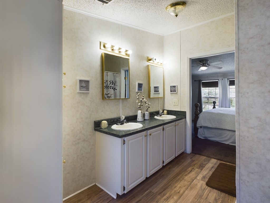 Double-sink bathroom vanity with illuminated mirrors and a bedroom visible through the doorway.