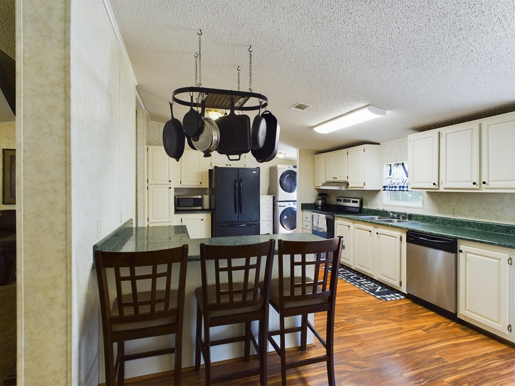 Kitchen with green countertops, a dark breakfast bar, hanging cookware, and white cabinets.
