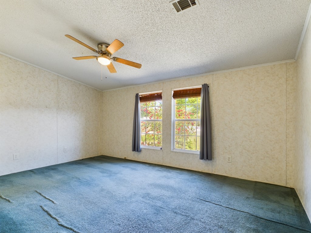 Empty bedroom with blue carpet, two curtained windows, and a ceiling fan.