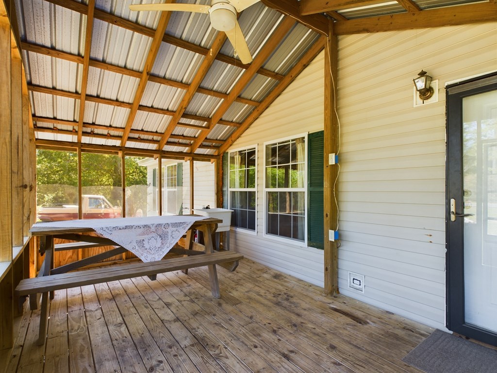 Covered wooden porch with exposed rafters, a picnic table, and windows along the house.