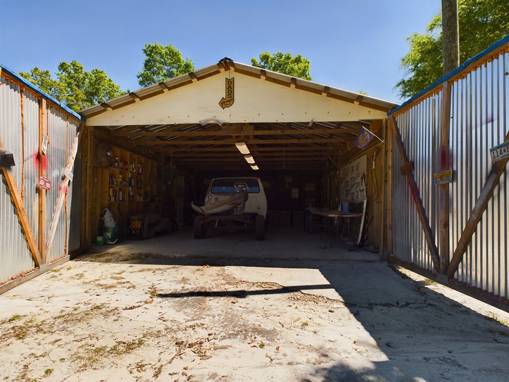 Open-front metal-sided garage with a pickup truck, boat, and concrete driveway.