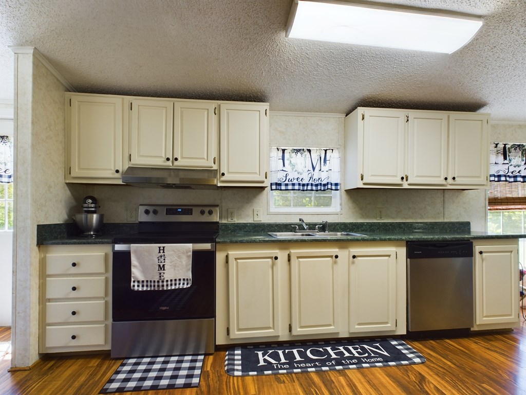 Kitchen with cream cabinets, green countertops, stainless-steel dishwasher, and hardwood floors.