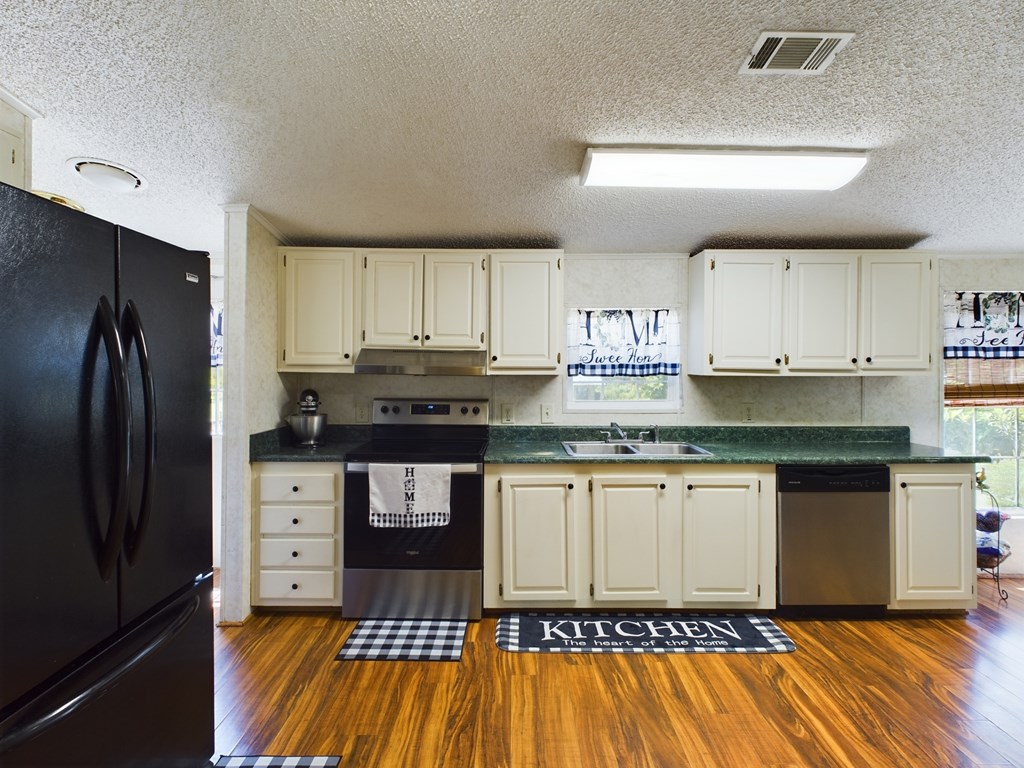 Kitchen with cream cabinets, green countertops, black appliances, and wood-look flooring.