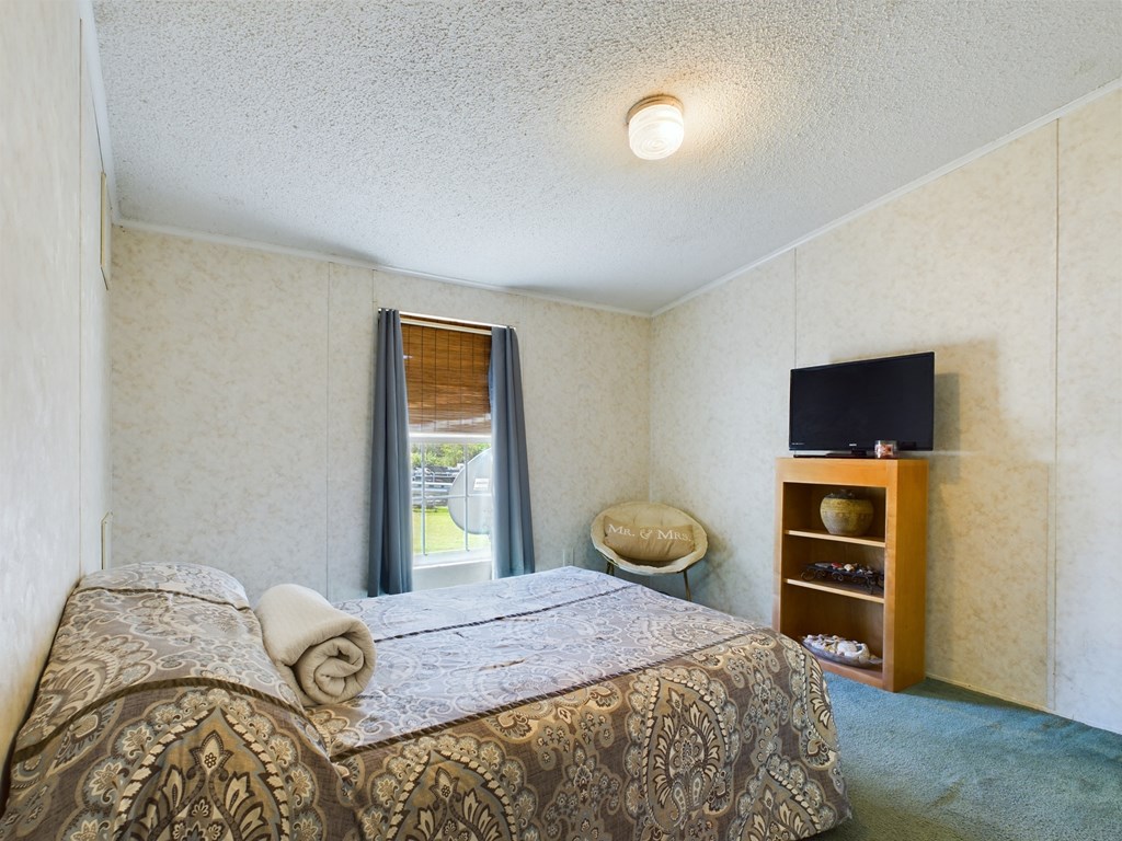 Bedroom with a patterned bedspread, blue curtains, and a television on a wooden shelf.