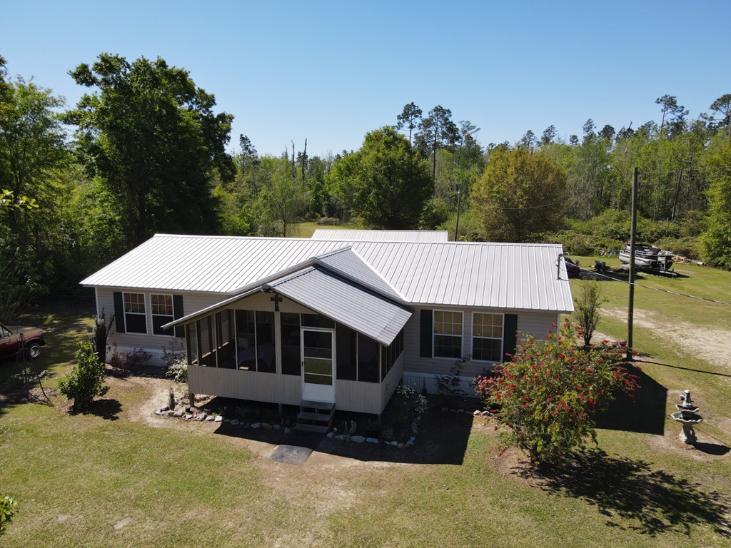 Gray single-story home with a metal roof and screened porch, surrounded by trees.