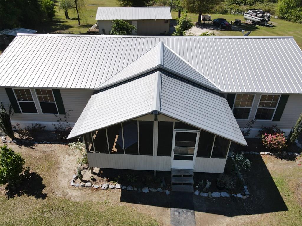 Aerial view of a single-story home with a metal roof and prominent screened front porch.